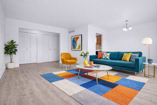 A living room with a blue couch, a yellow chair, a white coffee table, and a colorful rug.