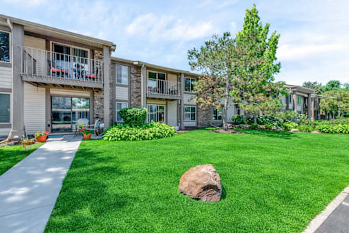 A large rock sits in the middle of a well-manicured lawn in front of a building.