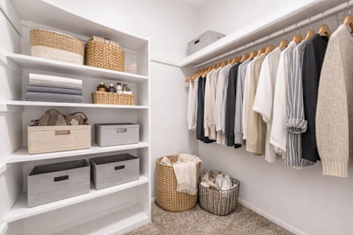A white closet with clothes hanging and baskets on the shelves.