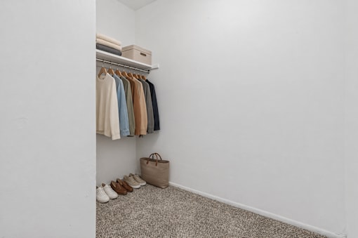 A closet with clothes hanging and shoes on the floor.