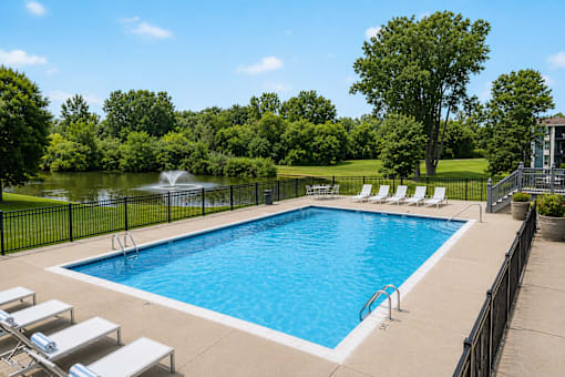 A pool surrounded by trees and lawn chairs.