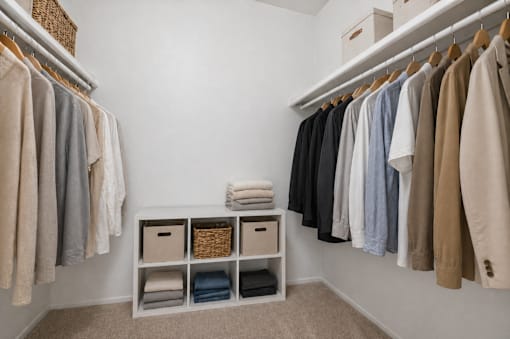 A white closet with clothes hanging and a basket on the shelf.