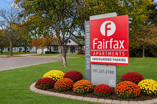 A sign for Fairfax Apartments with a tree and flowers in the foreground.