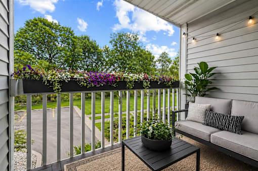 A balcony with a grey couch, a potted plant and a coffee table.