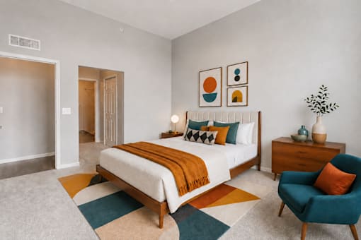 A bedroom with a bed, a chair, and a plant.
