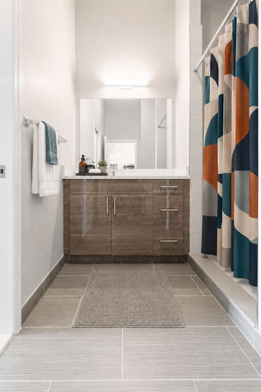 A bathroom with a brown cabinet and a patterned shower curtain.