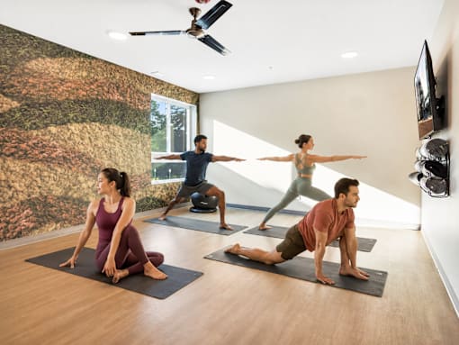 Three people doing yoga in a room with a wallpapered wall.