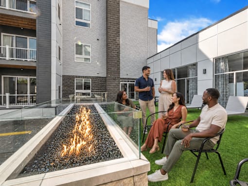 A group of people are sitting and standing around a fire pit on a patio.