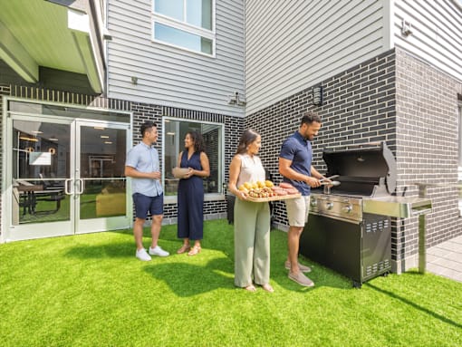 Three people are standing outside a house with a grill.