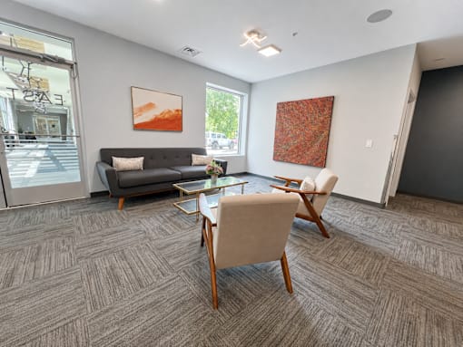 A living room with a grey sofa, a wooden table and chairs, and two pieces of artwork on the wall.