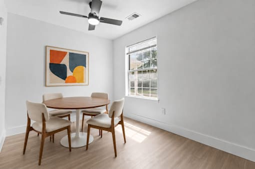 A dining room with a table and chairs and a painting on the wall.