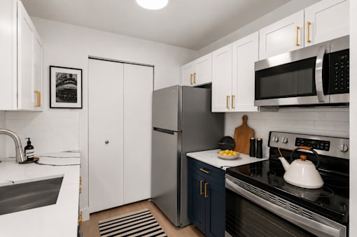 A modern kitchen with a stainless steel refrigerator and oven, white cabinets, and a black and white framed picture on the wall.