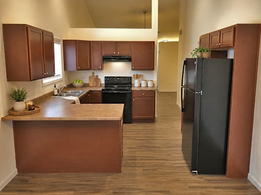 A kitchen with a black refrigerator and brown cabinets.