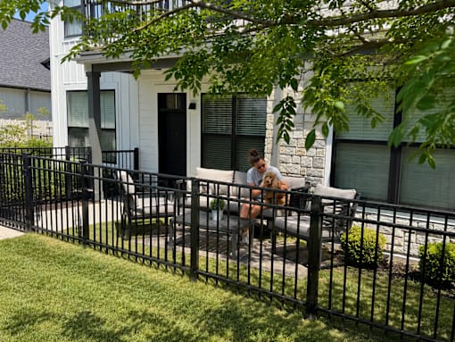 A woman is sitting on a bench with her dog in front of a white house.