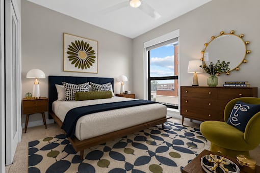 A bedroom with a bed, a chair, and a mirror.