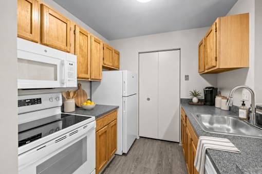 Kitchen with white appliances and oak cabinetry at Village Club of Farmington Hills Apartments, Farmington Hills, MI