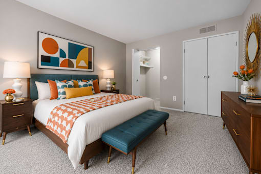Contemporary bedroom with colorful artwork and teal bench at Village Club of Farmington Hills Apartments, Farmington Hills, 48331