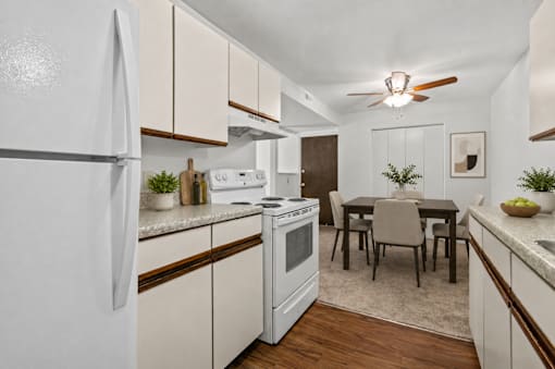 A white refrigerator stands in a kitchen with wooden cabinets and a dining table.