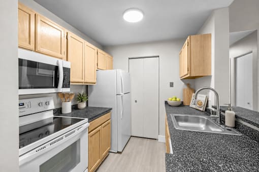 Galley kitchen with stainless steel sink and dark countertops at Village Club of Farmington Hills Apartments, Farmington Hills, MI