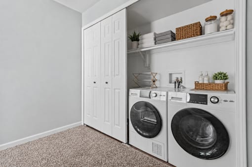 A laundry room with a washer and dryer and a shelf with decorative items.