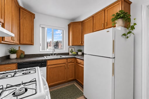 A white refrigerator stands in a kitchen with wooden cabinets and a window.