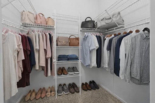 A white closet with clothes and shoes.