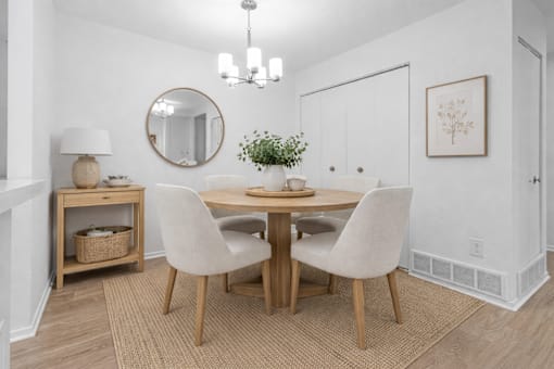 A dining room with a round mirror, a table with chairs, and a plant on the table.