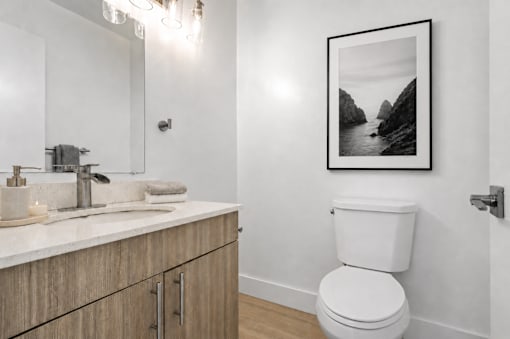 A bathroom with a toilet, sink, and a framed picture on the wall.