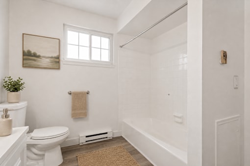 A white bathroom with a toilet, a sink, a window, and a rug.