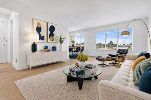 A living room with a white couch, a coffee table, and a large window with a view of the outside.