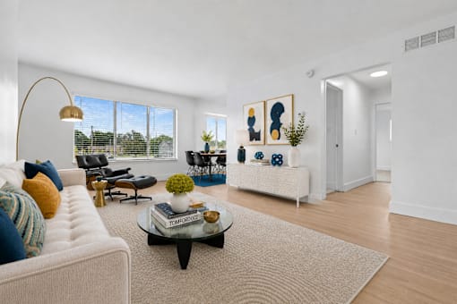 A living room with a white couch, a coffee table, and a large window.