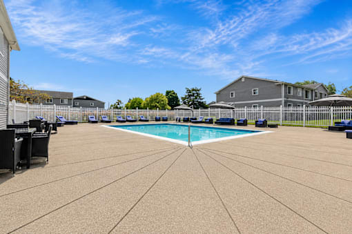 A large outdoor swimming pool surrounded by a concrete patio and a white fence.