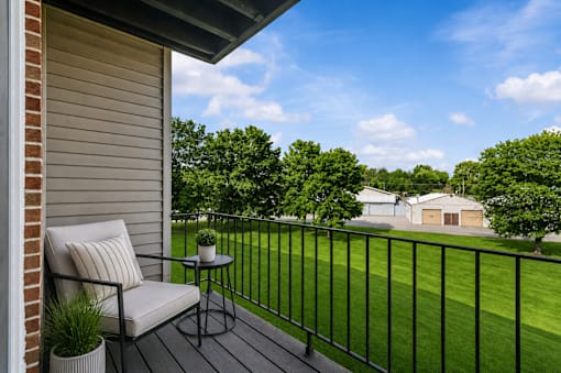 A balcony with a chair and table overlooking a green lawn.