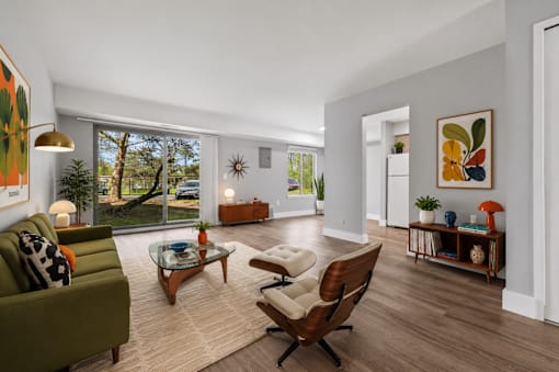 A living room with a green couch, a wooden chair, and a glass table.
