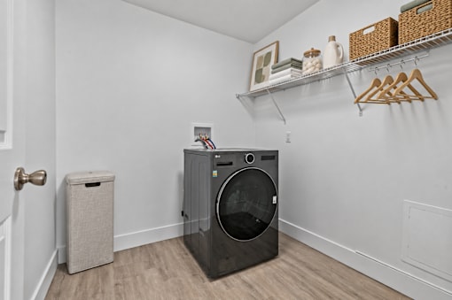 A black washing machine in a laundry room with a door and a trash can.