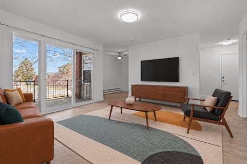 A living room with a brown leather couch, a wooden bench, and a television mounted on the wall.