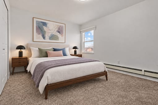 A bedroom with a bed, two lamps, and a painting on the wall.