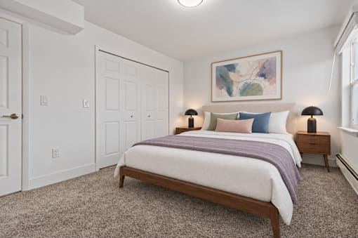 A bedroom with a bed, two lamps, and a painting on the wall.