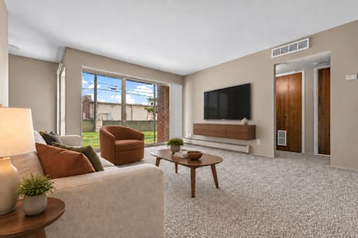 A living room with a white couch, a brown armchair, a wooden coffee table, and a flat-screen TV mounted on the wall.