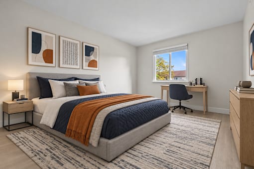 A bedroom with a large bed, a desk with a chair, and a window with a view of a tree and a building outside.