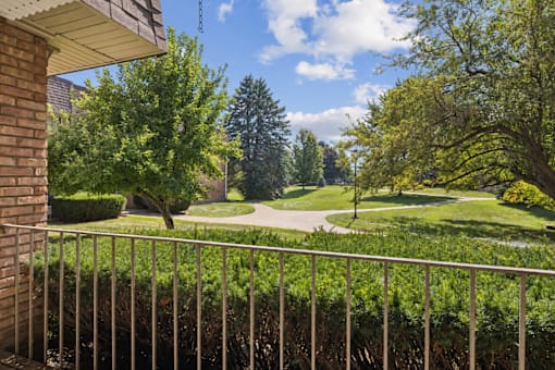 A view from a balcony looking out at a green lawn and trees.