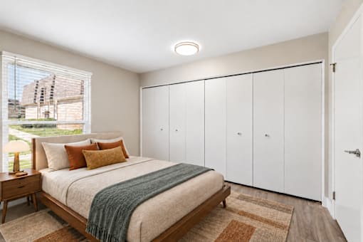 A bedroom with a bed, a nightstand, and a window with a view of a building outside.