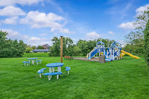 A playground with a blue and yellow slide, picnic tables, and a yellow slide.