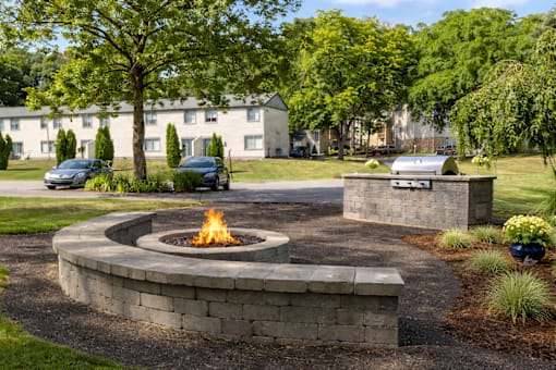 A fire pit in the middle of a grassy area with a building in the background.