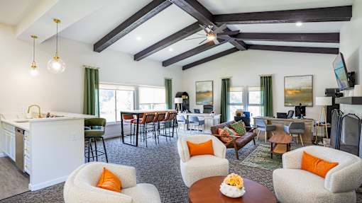 A living room with a white kitchen island and white chairs with orange pillows.