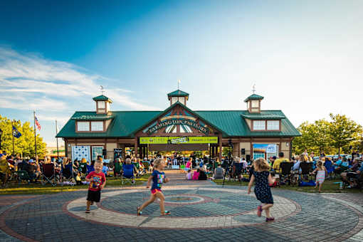 A group of people are dancing in a circle in front of a building with a green roof.