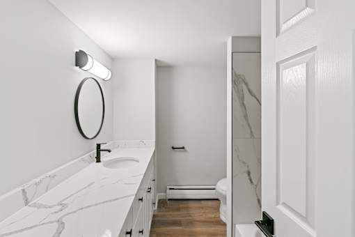 A white bathroom with a marble counter top and a round mirror. at The Park on 13 Apartments - Royal Oak, MI Apartments, Royal Oak, MI, 48073