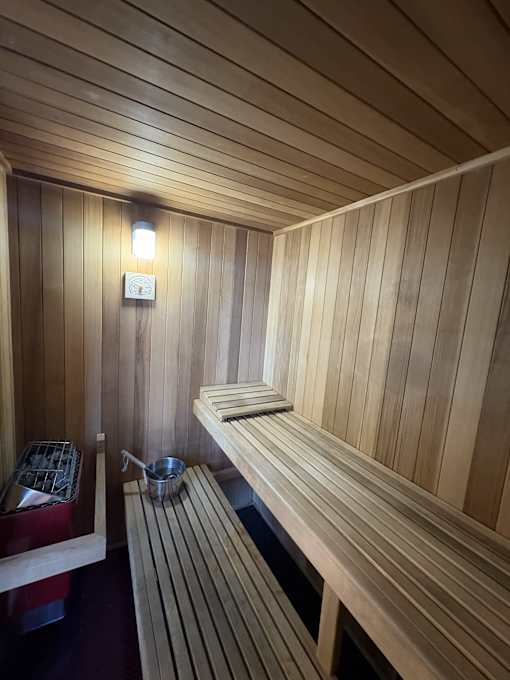 A wooden sauna with benches and a light on the wall.