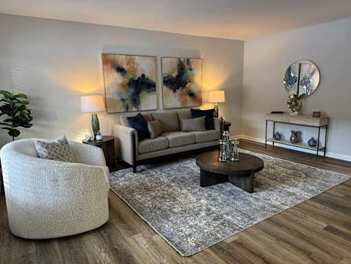 A modern living room with a grey sofa, a round chair, a coffee table, and a large abstract painting on the wall. at The Park on 13 Apartments - Royal Oak, MI Apartments, Royal Oak