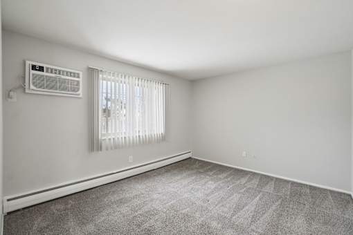 A room with a window covered by white blinds and a wall-mounted air conditioner unit.